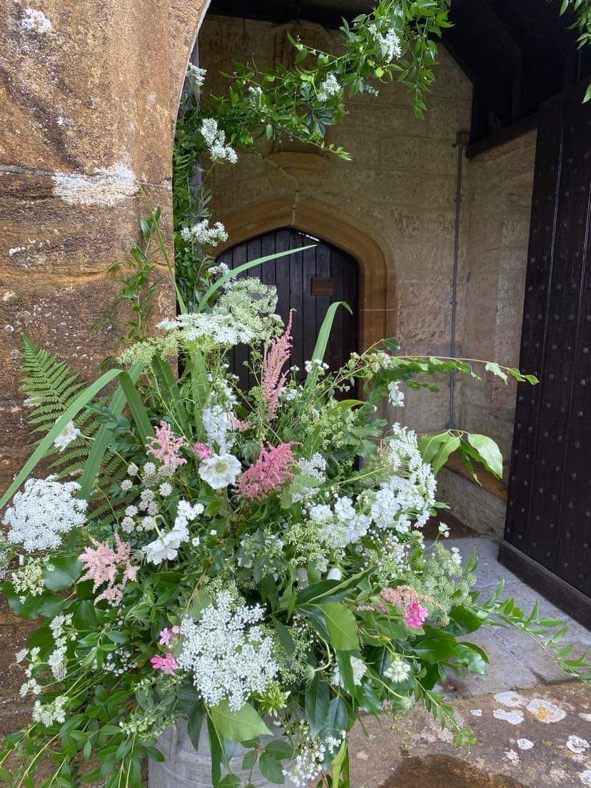 Large loose arrangement of Queen Anne's lace, pink astilbe and greenery in a stone church porch