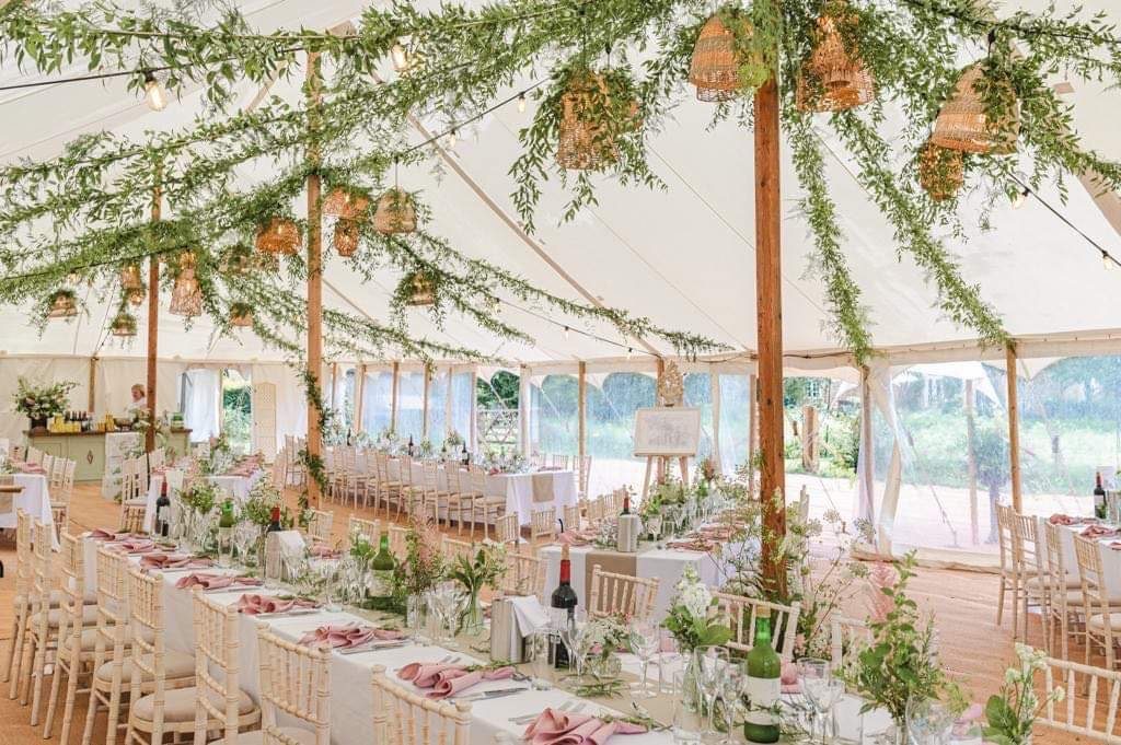 Marquee laid for a wedding breakfast with long tables and greenery hanging overhead