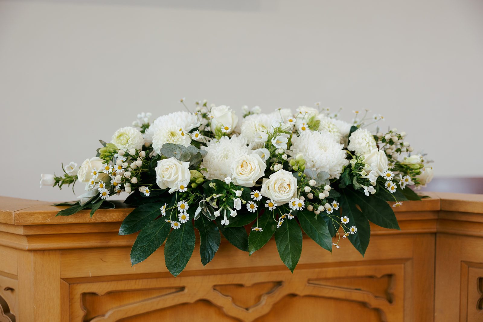 Long arrangement of white roses and foliage on a wooden ceremony table